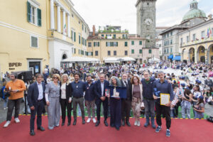 Foto di gruppo di finalisti ed organizzatori con al centro con il premio la vincitrice del 68° Bancarellino. Sullo sfondo una piazza della Repubblica invasa dai ragazzi. (Foto Walter Massari)